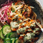 Crispy chicken, cucumbers, quinoa, and pickled red onions in a bowl with mint sauce and a fork