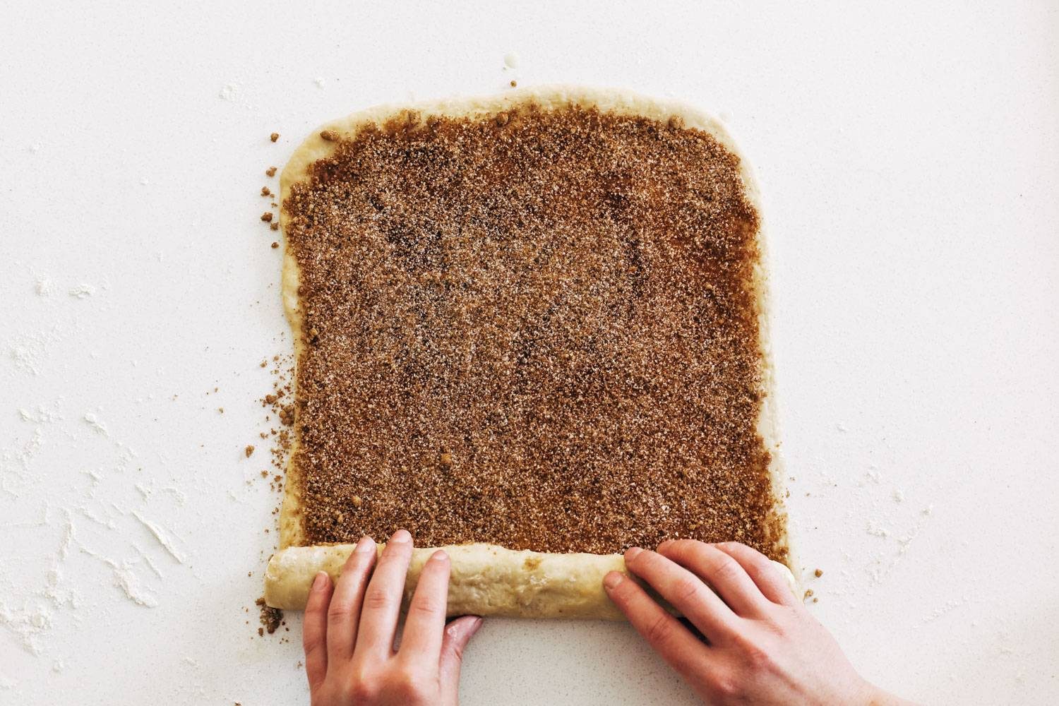 White hand rolling up cinnamon roll dough.
