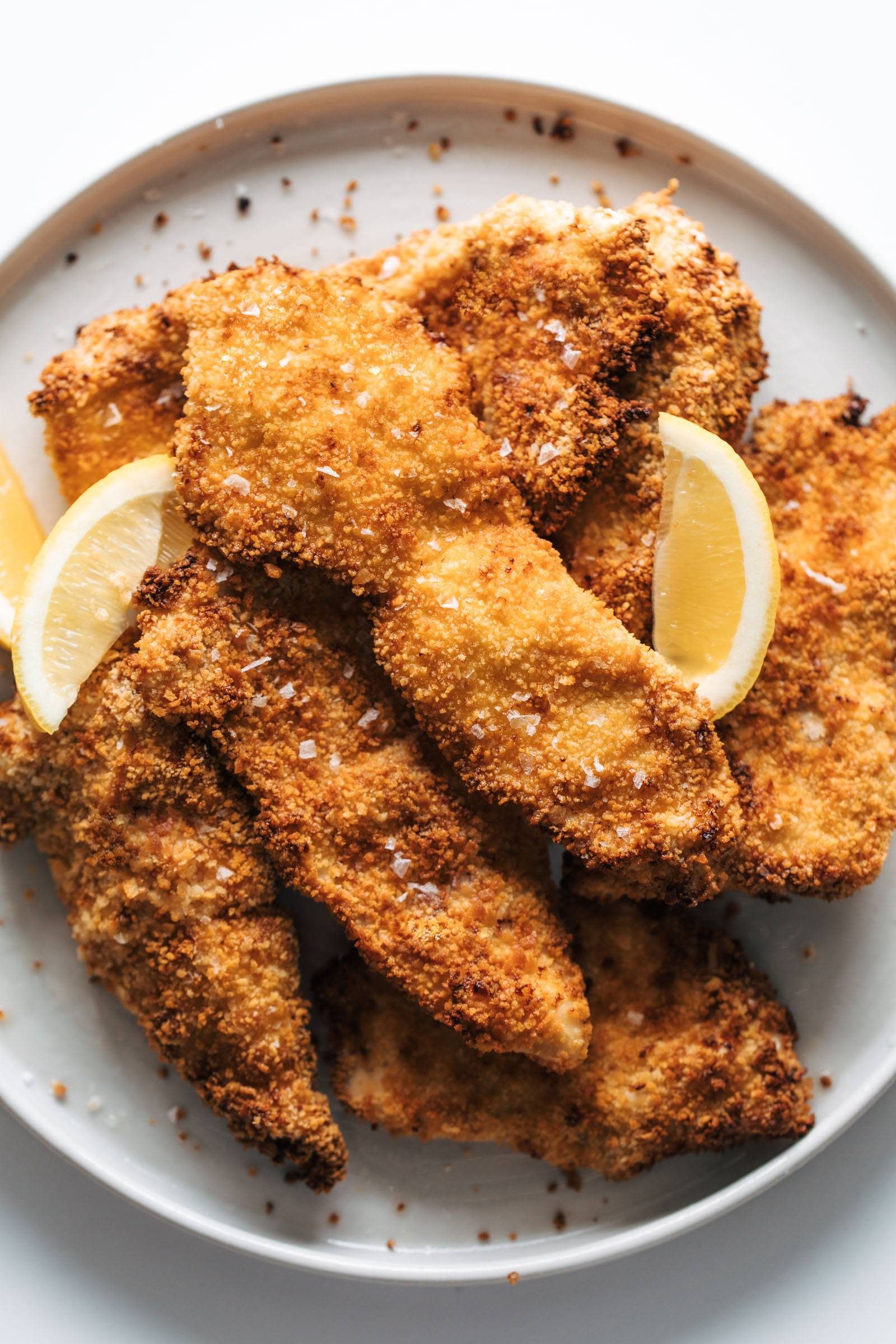 Crispy chicken cutlets on a plate with lemon slices.