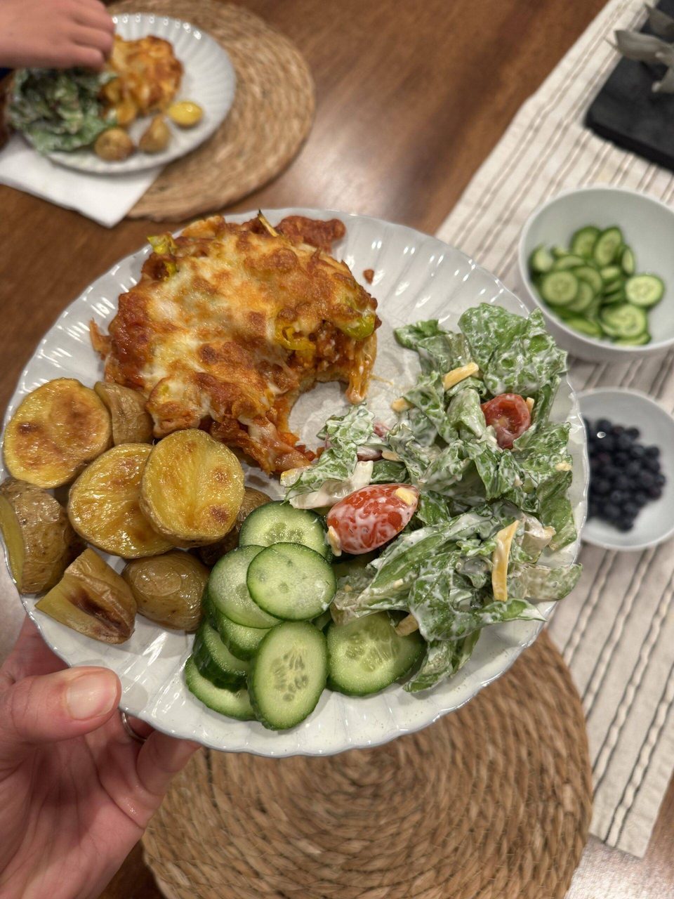 Pizza burger on a plate with potatoes, cucumber, and salad.