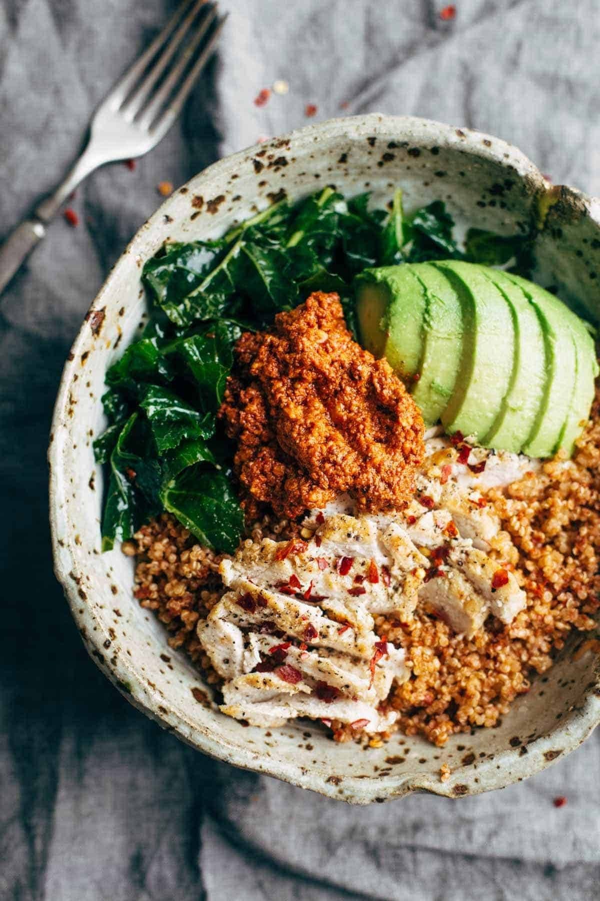 Chicken in a bowl with kale, quinoa, avocado and sun-dried tomato sauce.