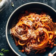 White hand holding a bowl of saucy noodles.