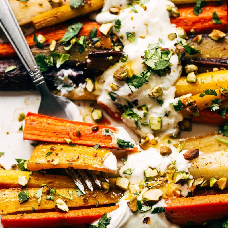 Heirloom carrots on a sheet pan with yogurt sauce and a fork.