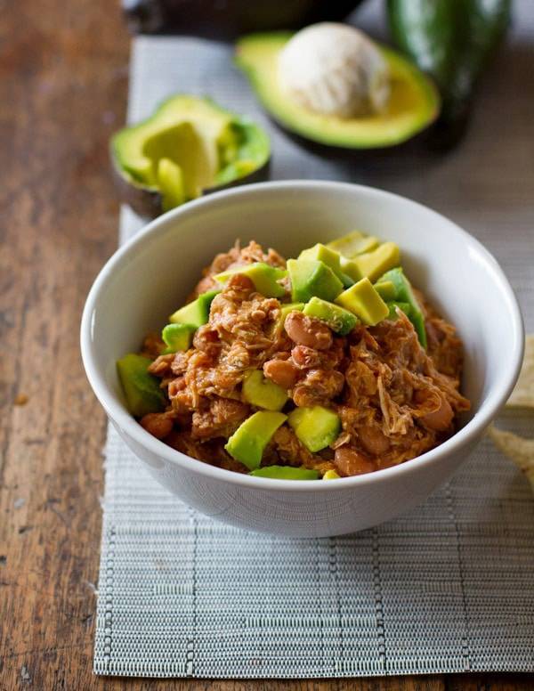 Mexican chicken and pinto beans in a white bowl with avocado. 